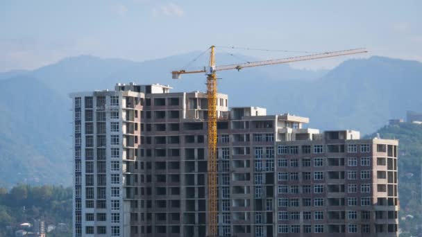 O guindaste da torre em um canteiro de obras levanta uma carga no edifício alto. Prazo de validade — Vídeo de Stock