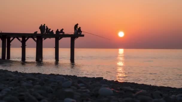 Siluetas de pescadores con cañas de pescar al atardecer en el muelle. Moción lenta . — Vídeo de stock