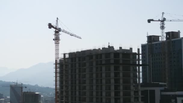 Construção civil. Timelapse. Guindastes de torre em um canteiro de obras eleva uma carga no prédio de arranha-céus . — Vídeo de Stock