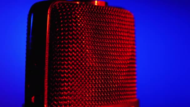 Micrófono de condensador gira con luz de fondo azul y rojo. Grabadora de audio profesional Primer plano — Vídeo de stock
