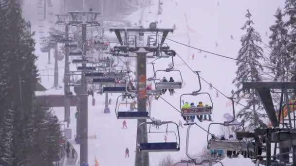 Ski Lift on Ski Resort. Skiers Climb on a Ski Chair Elevator up to Ski Slope with Falling Snow — Stock Video