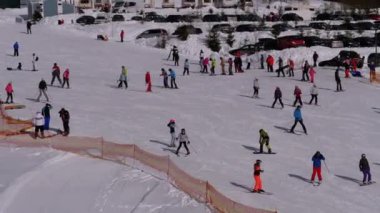 Kayakçılar ve Snowboardcular güneşli bir günde karlı bir yamaçta geziyorlar.