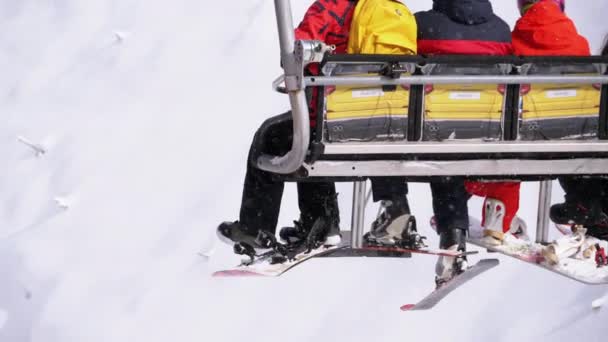 チェアリフトに乗って4人のスキーヤーとスノーボーダーが登ります。スキー場。スローモーション — ストック動画
