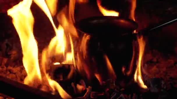 Турку с кофейником готовят в огне, стоя на углях, обнятых языками красного пламени — стоковое видео