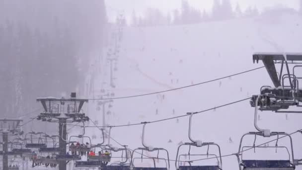Skidlift på skidorten. Skidåkare Klättra på en skidstol Hiss upp till skidbacken med fallande snö — Stockvideo