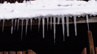 Icicles Melt and Dripping on the Sun Hanging from the Roof of Wooden House. Slow Motion