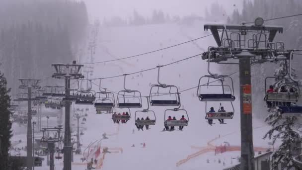 Skilift auf Skigebiet. Skifahrer steigen im Sessellift auf Skipiste mit fallendem Schnee — Stockvideo