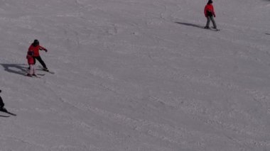 Kayakçılar ve Snowboardcular güneşli bir günde karlı bir yamaçta geziyorlar.