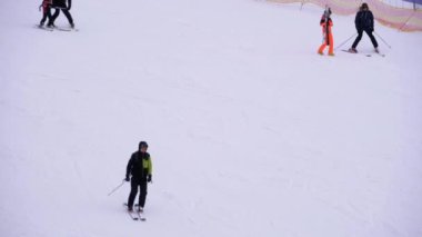 Kayakçılar ve Snowboardcular güneşli bir günde karlı bir yamaçta geziyorlar.