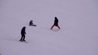 Kayakçılar ve Snowboardcular güneşli bir günde karlı bir yamaçta geziyorlar.
