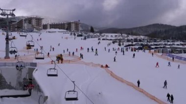 Kayakçılar ve Snowboardcular güneşli bir günde karlı bir yamaçta geziyorlar.