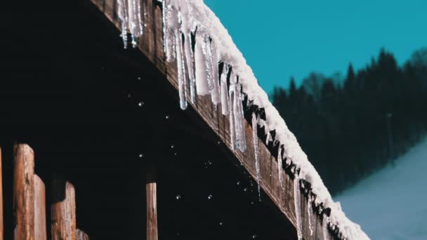 Icicles Melt and Dripping on the Sun Hanging from the Roof of Wooden House. Slow Motion — Stock video