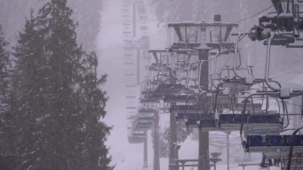 Remonte en estación de esquí, cámara lenta. Esquiadores suben en el elevador de la silla de esquí a la pista de esquí con nieve cayendo — Vídeo de stock