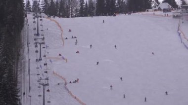 Kayakçılar ve Snowboardcular güneşli bir günde karlı bir yamaçta geziyorlar.