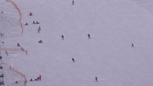 Les skieurs et les snowboarders montent sur une piste enneigée dans une station de ski en journée ensoleillée — Video