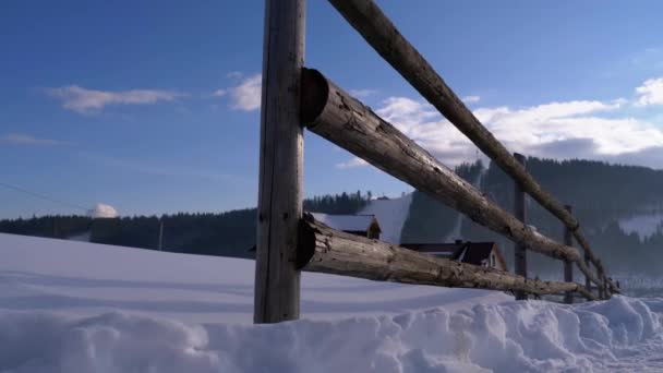 Cena rural de inverno com cerca de madeira abandonada velha e casa de madeira nevada e montanhas — Vídeo de Stock