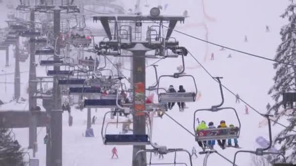 Skilift auf Skigebiet. Skifahrer steigen im Sessellift auf Skipiste mit fallendem Schnee — Stockvideo