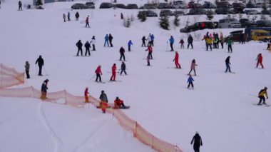 Kayakçılar ve Snowboardcular güneşli bir günde karlı bir yamaçta geziyorlar.