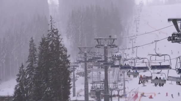 Skilift auf Skigebiet. Skifahrer steigen im Sessellift auf Skipiste mit fallendem Schnee — Stockvideo