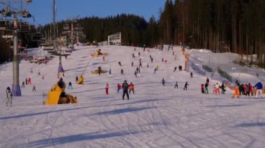 Kayakçılar ve Snowboardcular güneşli bir günde karlı bir yamaçta geziyorlar.