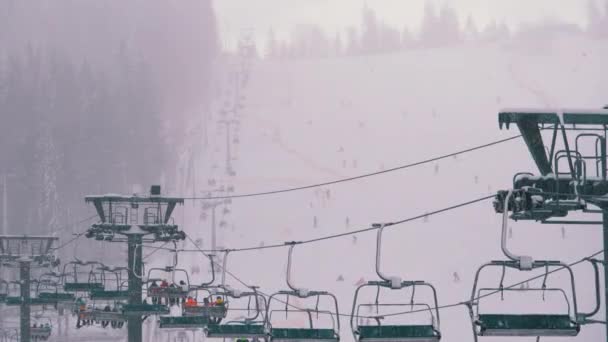 Lyžařský vlek na lyžařském středisku. Lyžaři vylezou na sedačkovou lanovku až na sjezdovku s padajícím sněhem — Stock video
