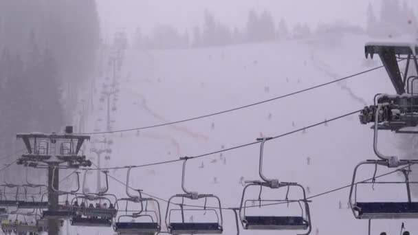 Ski Lift on Ski Resort. Skiers Climb on a Ski Chair Elevator up to Ski Slope with Falling Snow — Stock Video