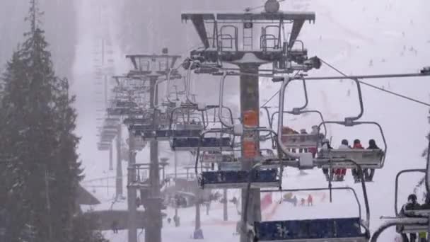 Remonte en la estación de esquí. Esquiadores suben a un elevador de la silla de esquí hasta la pista de esquí con nieve cayendo — Vídeo de stock