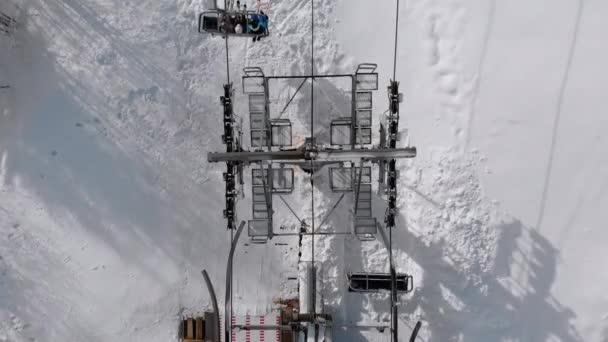 Vista aerea dall'alto dell'impianto di risalita per gli sciatori da trasporto sulla pista da sci innevata. Drone vola sopra la sedia ascensore — Video Stock