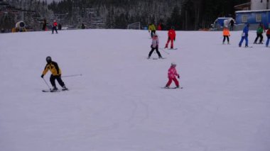Kayakçılar ve Snowboardcular güneşli bir günde karlı bir yamaçta geziyorlar.