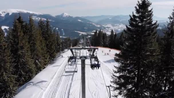 Drone vola sopra gli impianti di risalita e pista da sci innevata con sciatori in cima alla montagna — Video Stock