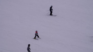 Kayakçılar ve Snowboardcular güneşli bir günde karlı bir yamaçta geziyorlar.