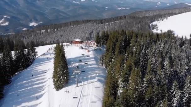 Piste da sci aeree con sciatori e impianti di risalita sulla stazione sciistica. Foresta montana innevata — Video Stock