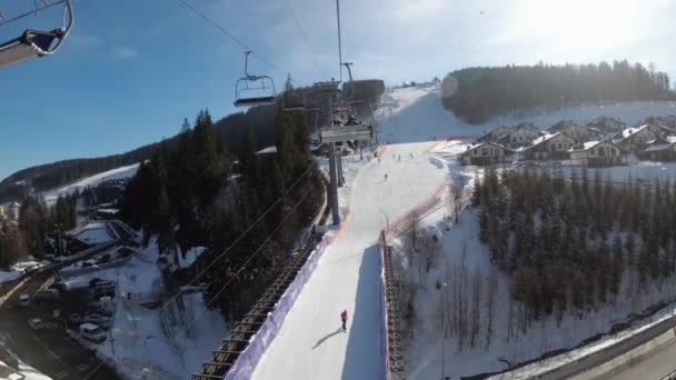 POV desde telesilla de esquí bajo estación de esquí y pista de esquí nevada con esquiadores — Vídeos de Stock