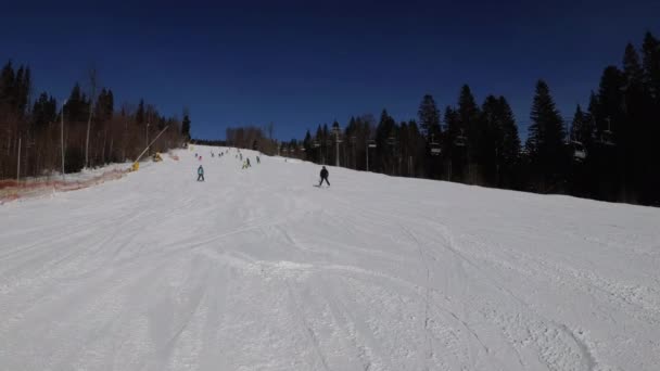 Förstapersonsvy på skidåkare och snowboardåkare glider ner på skidbacken på skidorten — Stockvideo