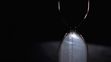 Siyah bir arkaplanda kum saati. Yakın plan. Kum saati boyunca hareket eder.