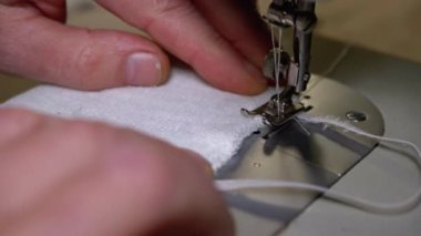Dikiş Makinesindeki Terzi Covid-19 'u korumak için Ev Yapımı Tıbbi Yüz Maskesi Dikiyor