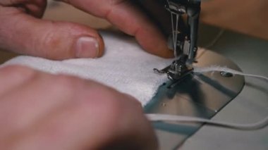 Dikiş Makinesindeki Terzi Covid-19 'u korumak için Ev Yapımı Tıbbi Yüz Maskesi Dikiyor