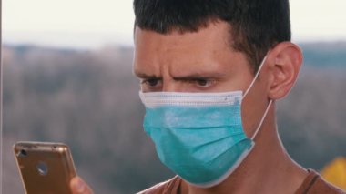 Koruyucu Yüz Maskeli Adam Akıllı Telefona bakar ve onu Sokakta Eller 'de tutar.