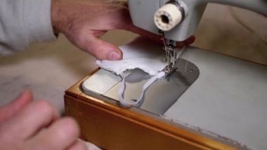 Dikiş Makinesindeki Terzi Covid-19 'u korumak için Ev Yapımı Tıbbi Yüz Maskesi Dikiyor