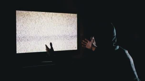 Hombre de silueta en capucha y máscara médica viendo la interferencia de la televisión con las manos arriba — Vídeos de Stock