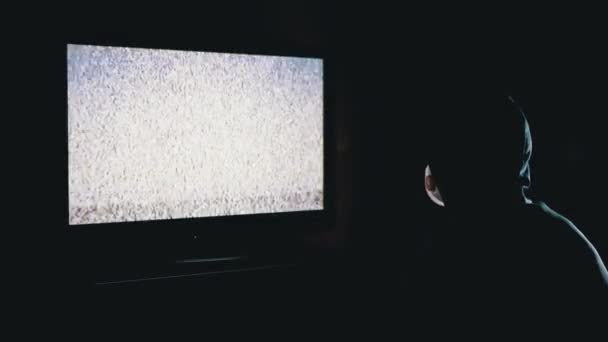 Σιλουέτα του ανθρώπου στην κουκούλα και ιατρική μάσκα βλέποντας τηλεόραση με στατική παρέμβαση — Αρχείο Βίντεο