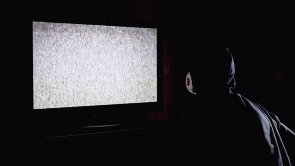 Fake News. Silhouette eines Mannes mit Kapuze und medizinischer Maske, der Fernsehstörungen beobachtet — Stockvideo