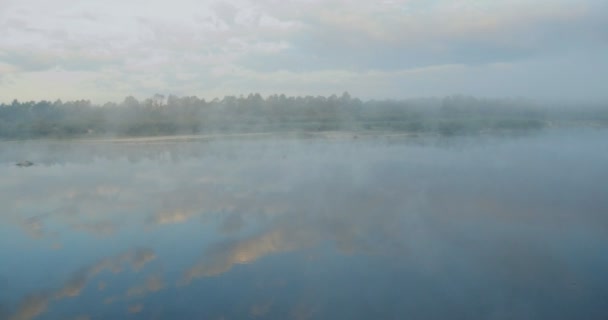 在平静的河流上空低空飞行 浓雾笼罩在水面上 太阳从树后升起 平静的水 树木反映在水中 清晨的薄雾传遍了河水 — 图库视频影像