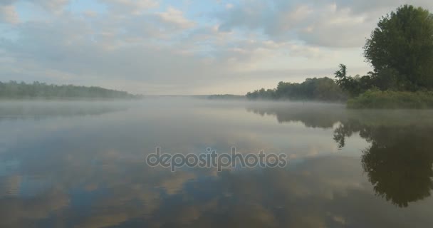 在平静的河流上空低空飞行 浓雾笼罩在水面上 太阳从树后升起 平静的水 树木反映在水中 清晨的薄雾传遍了河水 — 图库视频影像