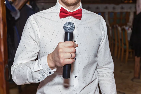 Master of ceremonies in a white shirt and with a red butterfly holding a microphone in his hand, Master of ceremonies with microphone