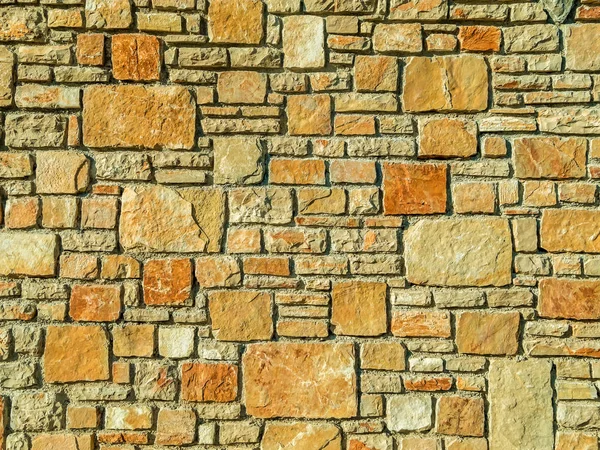 Wall of orange and beige stones. Stone wall.