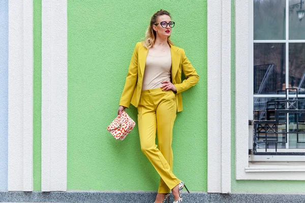 Элегантная женщина в жёлтом костюме на фоне зелёной стены — стоковое фото