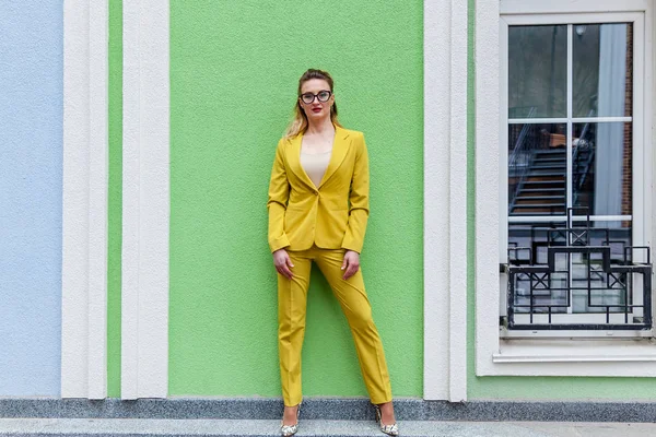 Элегантная женщина в жёлтом костюме на фоне зелёной стены — стоковое фото