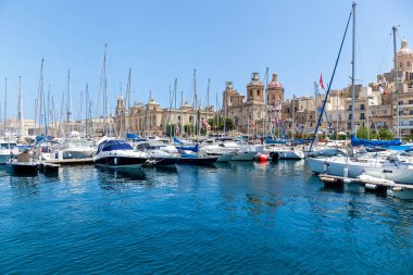 Limanda, Malta şehrinin arka planında güneşli bir yaz gününde eski binalar ve palmiye ağaçları olan bir sürü demirli yat var..