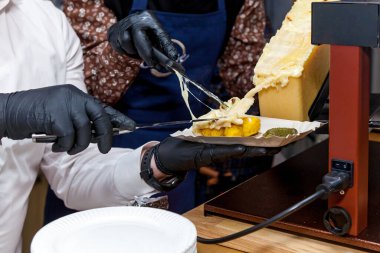 Bir şef, peynirleri eritmek için özel bir enstrüman kullanarak raclette yemek hazırlıyor..